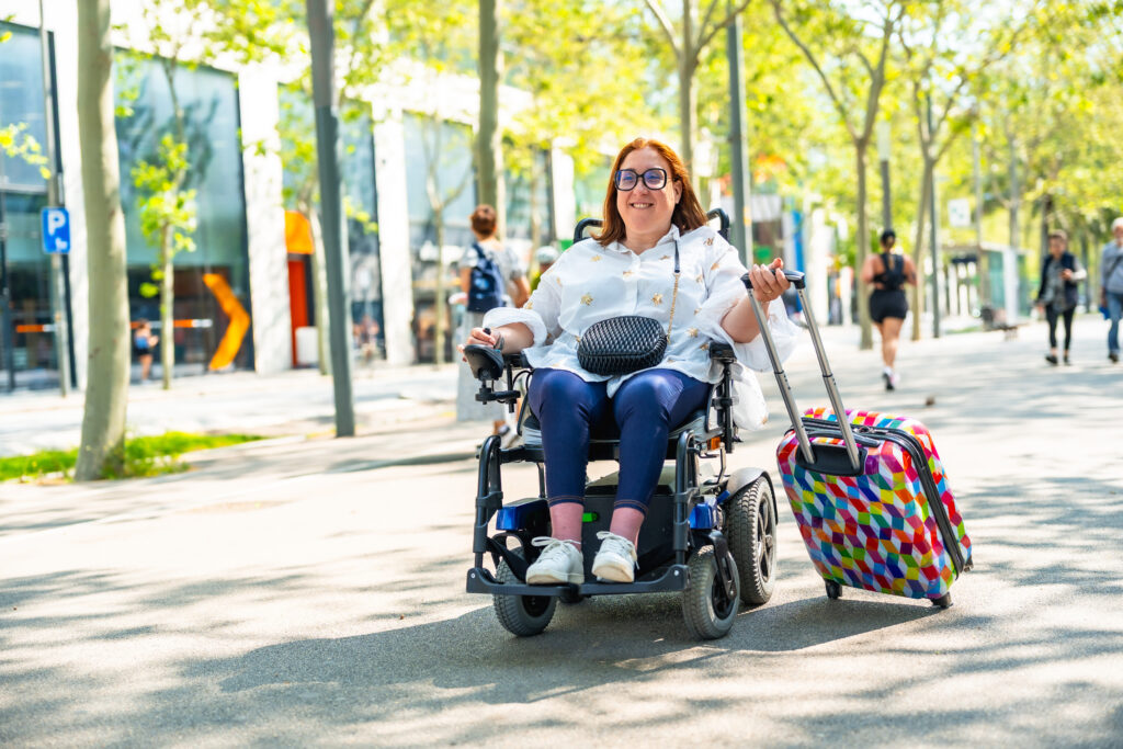 happy tourist with disability traveling with suitcase using a wheelchair in urban park