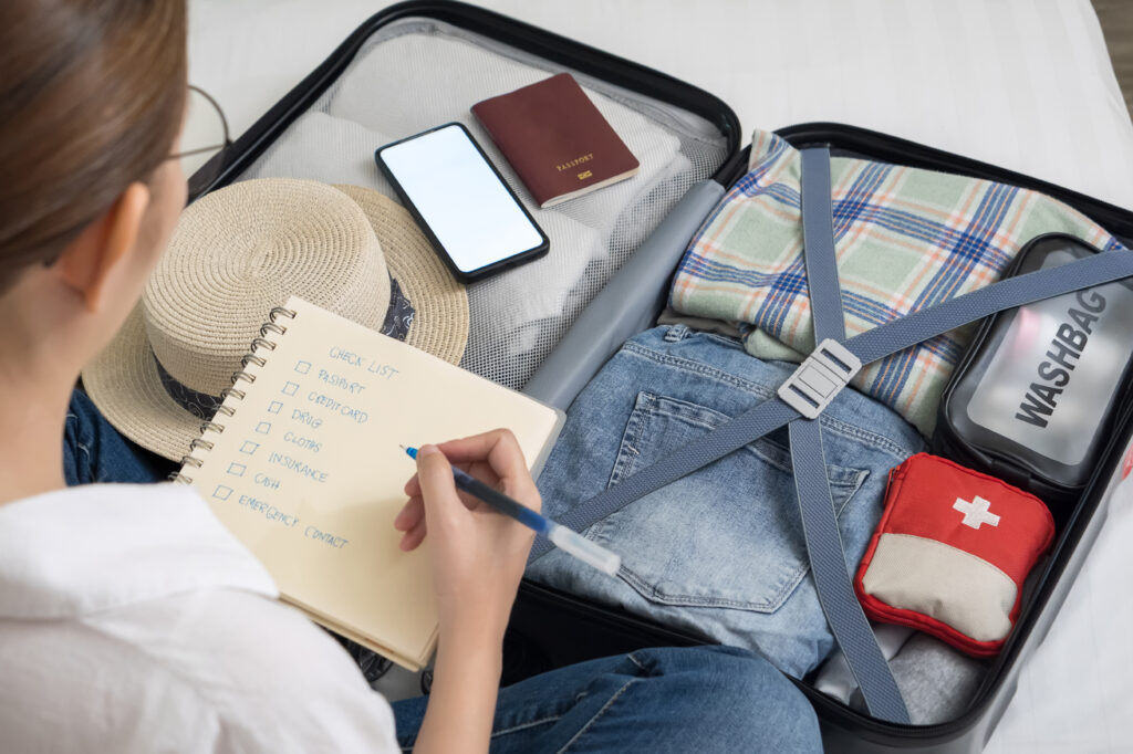 Packing Tips for Mature Travellers making a check list of things to pack for travel. woman writing checklist item on notebook and packing suitcase to vacation, prepare clothes, medicine, passport into luggage. travel vacation concept