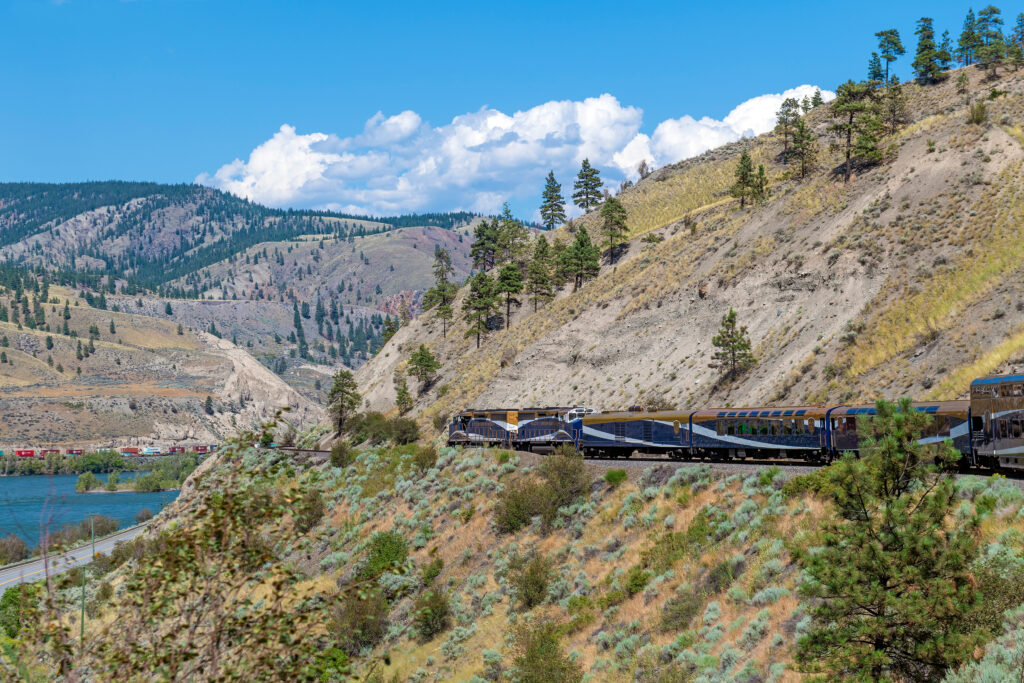 Welcome to Infinite Journeys rocky mountaineer locomotive with gold and silver leaf train wagons along fraser river, british columbia, canada